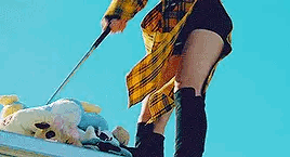 A gif of Yves hitting a golf club into a stack of stuffed animals, on top of a roof, against a blue sky.